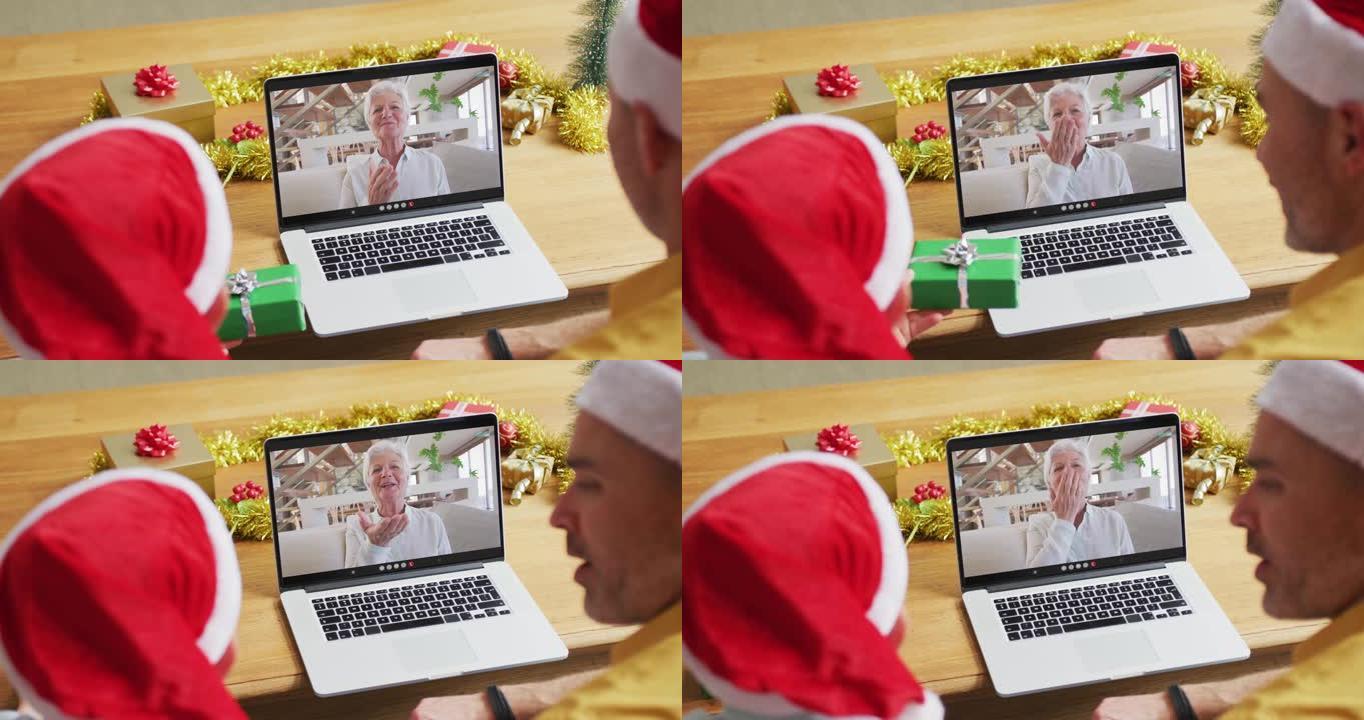白人父亲和儿子戴着圣诞老人的帽子，使用笔记本电脑与屏幕上的女人进行圣诞节视频通话