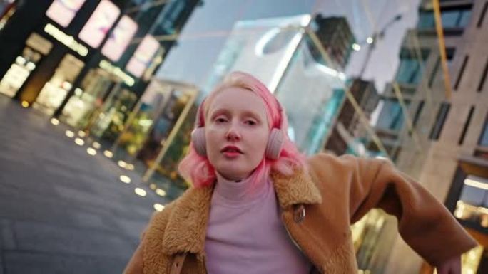 晚上在现代商业区跳舞的粉红色发型的年轻无忧无虑的女人的特写肖像，跟踪镜头