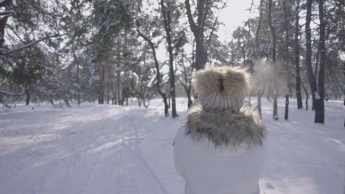 穿着冬季羽绒服的女孩在白雪皑皑的冬季森林中漫步。年轻女子高兴地微笑着环顾四周。森林里有很多雪。下雪的
