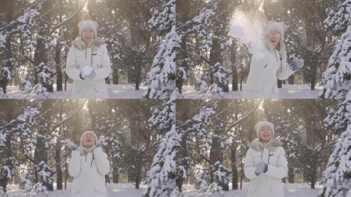 快乐可爱的女孩穿着冬装，对着镜头扔雪球，开心地笑着。下雪的冬天，阳光灿烂。美丽的模糊背景雪域自然松林