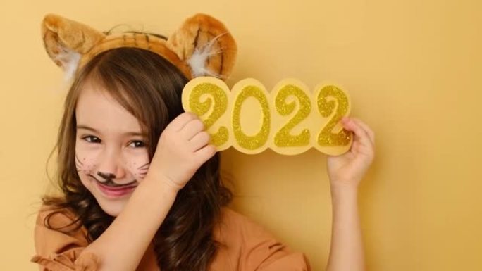 漂亮的女孩与耳朵和画脸的形象的老虎拿着辉煌的数字2022新年在她的手中。