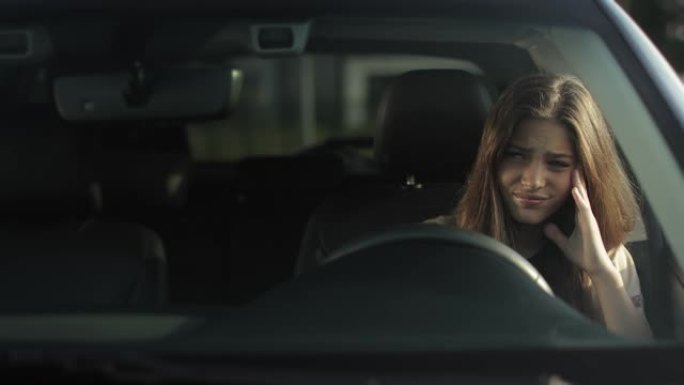 一个疲倦的女人坐在驾驶座上。她在等人，靠在门上。阳光照在她身上。4K