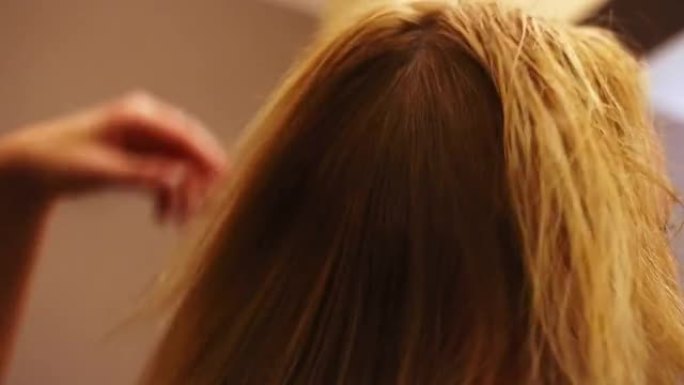 理发师吹干她客户刚洗过的头发。她用手穿过头发以松开头发。摄像机从侧面看