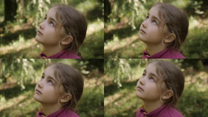 孩子抬头看着大自然的天空。肖像小女孩祈祷着带着希望和信念仰望天空，沉思的孩子脸，特写镜头。女孩仰望上