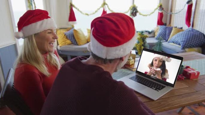 微笑的高加索夫妇戴着圣诞老人的帽子，使用笔记本电脑与屏幕上的女人进行圣诞节视频通话