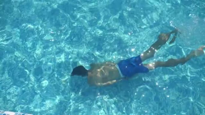 穿着短裤的黑发男孩在slo-mo的浅蓝色涉水池中水下游泳
