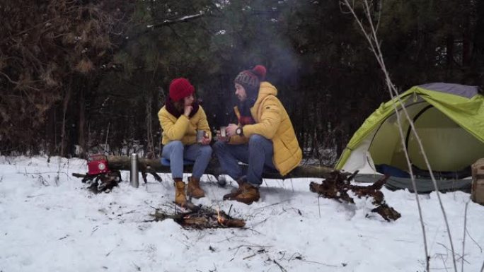 青年男女在冬日森林的炉火旁喝茶