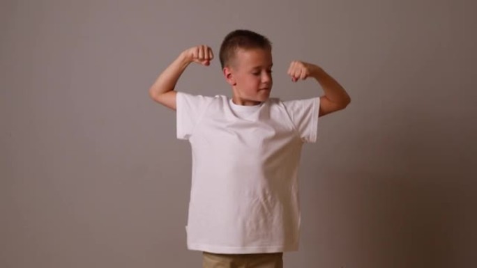 这个男孩展示了他手臂上的肌肉。强壮的男孩。一吨背景上穿着白色t恤的孩子