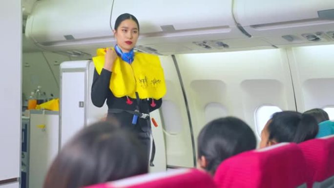 亚洲空姐解释并展示起飞前在飞机上抛弃时使用救生衣的安全演示。机组人员在飞行过程中演示乘客安全。