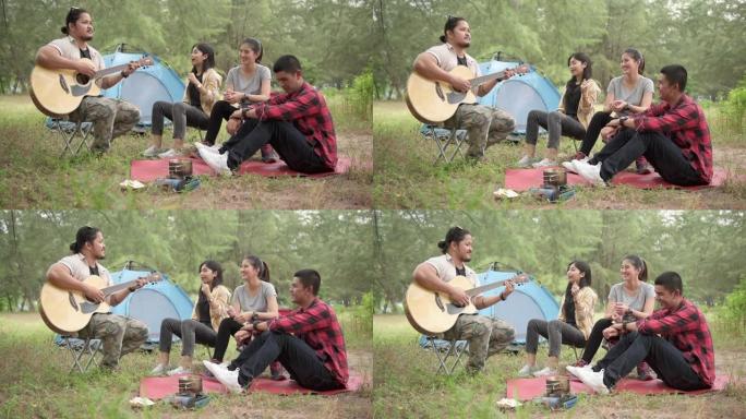 徒步旅行和露营概念。一群四个亚洲青少年在树林里露营时唱歌和弹吉他。