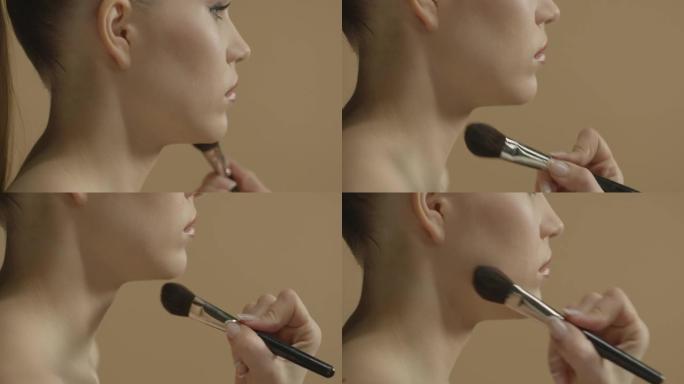 化妆师用化妆刷在一个年轻美丽的女孩脸上扑粉。