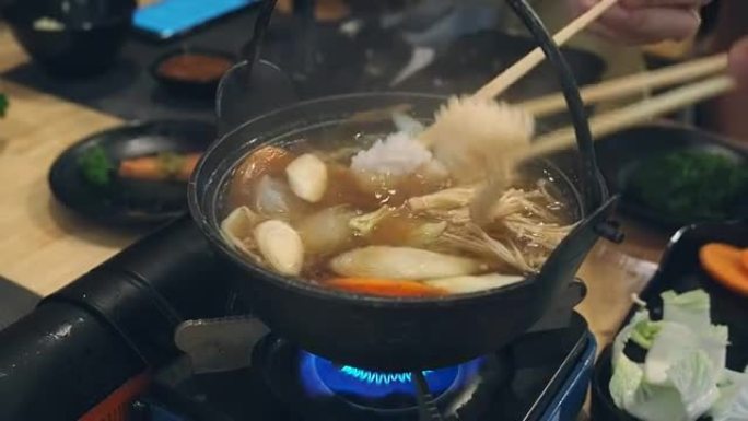 那人用筷子把鱿鱼从锅里拿出来。一家人在一家日本餐厅吃sha锅晚餐。与家人一起吃sha锅。
