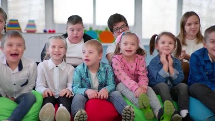 残疾儿童花时间与健康的孩子，男孩和女孩坐在豆袋椅上对着镜头微笑