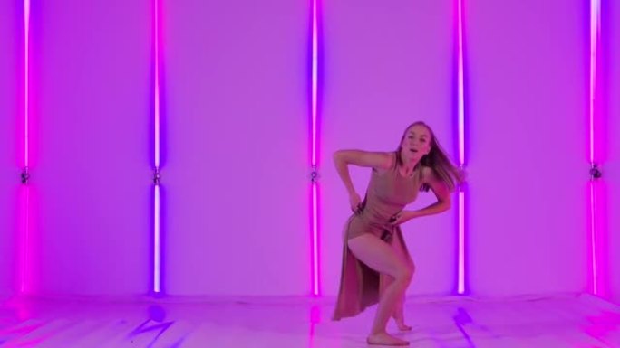 女性舞者表现出感性的蔑视，并在明亮的霓虹灯的背景下优雅地跳跃。年轻女子在黑暗的工作室里跳舞现代舞蹈。