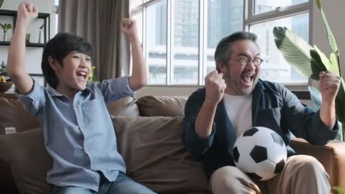 亚洲父子在电视上观看足球比赛，并在球队将球射入球门时做出高兴的反应。