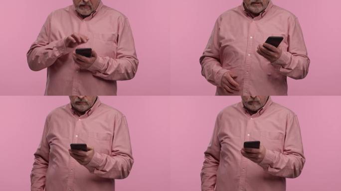 一个戴着眼镜的老人在手机上发短信的肖像。灰发的养老金领取者祖父，留着胡须，穿着衬衫，在粉红色的工作室