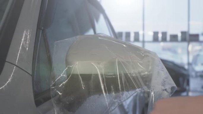 工人用手在汽车后视镜上包裹湿油漆保护膜或抗砾石保护涂层。汽车细节