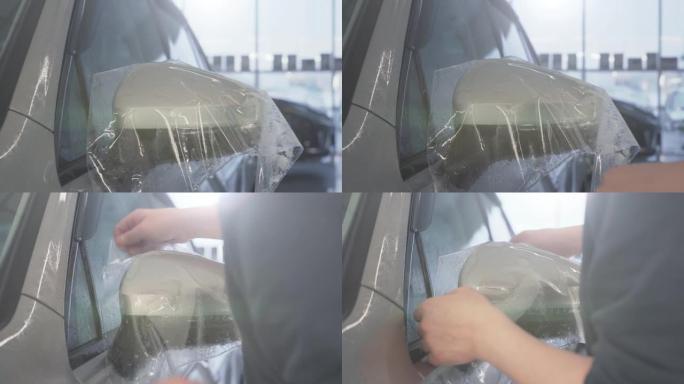 工人用手在汽车后视镜上包裹湿油漆保护膜或抗砾石保护涂层。汽车细节