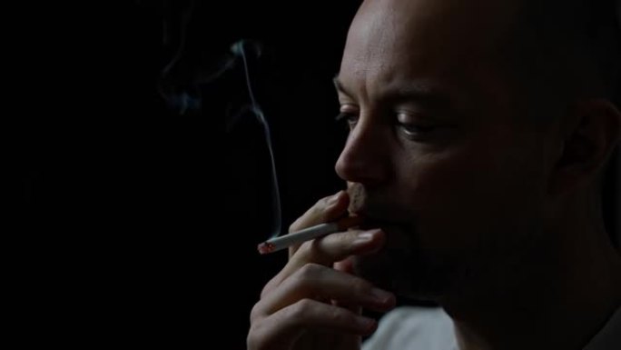 男人抽着烟，从嘴里吹出烟。孤立在黑色背景上，景深浅。