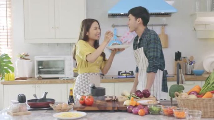 恋爱中的年轻夫妇在家里浪漫的气氛中帮忙做饭，带着微笑的脸看着相机。