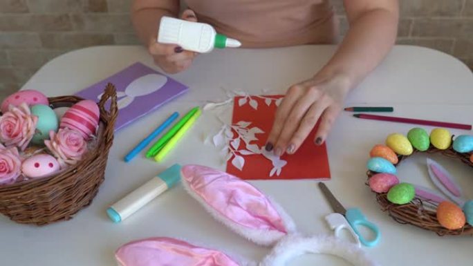 女人为复活节做工艺品。彩色纸制作的彩色手工卡片。剪刀，纸板，鸡蛋，兔子。木桌上的艺术创意