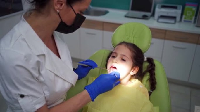勇敢的孩子坐在牙医的椅子上，而女牙医使用牙医的探针进行检查