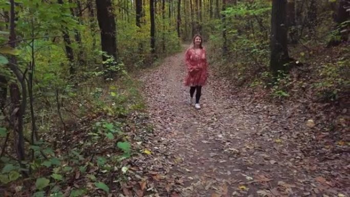 孕妇在秋天与可卡犬在公园小径上行走