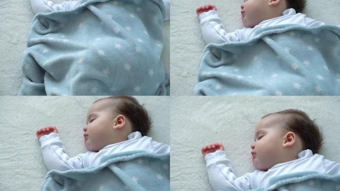 可爱的高加索小婴儿胖乎乎的小女孩的真实特写，睡在舒适的白色床上，铺着蓝色毯子。儿童保育，熟睡的婴儿，