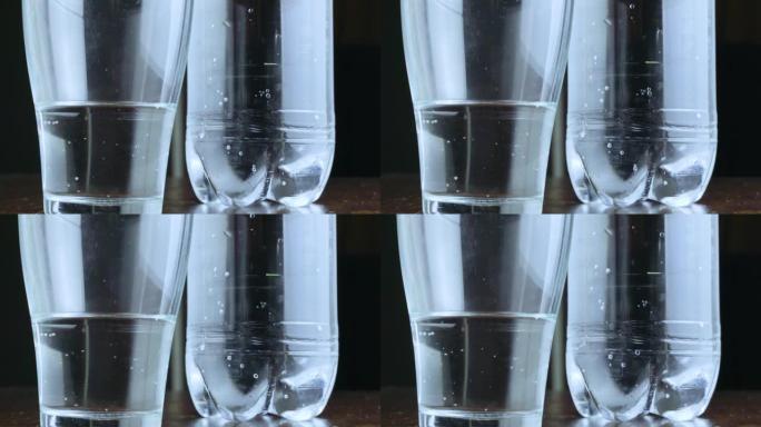在黑暗背景上的玻璃杯中闪闪发光的矿泉水，背景是一瓶水。一瓶苏打水或苏打水。口渴。饮酒制度和平衡。健康