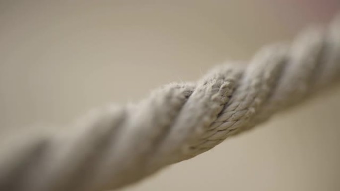 模糊的米色背景上的绳子的极端特写。行动。拉伸的米色绳索的宏观视图，相机焦点沿着绳索缓慢滑动