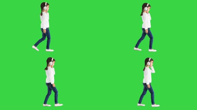 穿着白色衣服的小女孩戴着耳机走路，对着绿色屏幕上的音乐节拍点了点头，色键