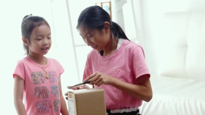 快乐的亚洲儿童收到了网上购物的商品，并在家里的窗户附近打开了棕色盒子，生活方式理念。