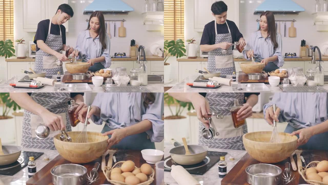 亚洲夫妇在家里的厨房里互相帮助，在浪漫的气氛中制作面包店。年轻女性用微笑和快乐的面孔帮助烹饪假期。
