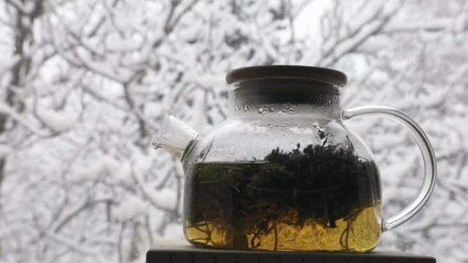 飘雪背景下的带有芳香草药的玻璃茶壶