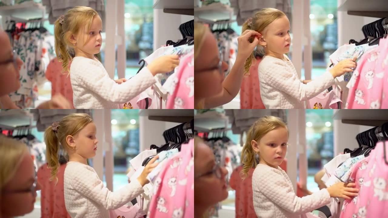 购物快乐的家庭。商场里的家庭。母亲帮助女儿在童装商店中选择衣服。选择一个婴儿手提包。与母亲在购物中心