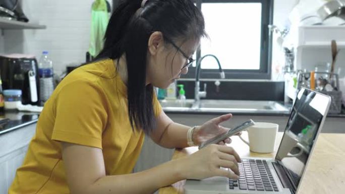 亚洲女性在厨房里使用笔记本电脑和智能手机。