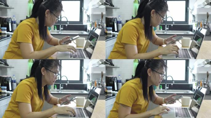 亚洲女性在厨房里使用笔记本电脑和智能手机。