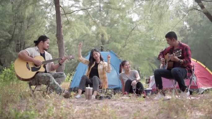 徒步旅行和露营概念。四名亚洲男女在树林里露营，唱歌和弹吉他很有趣。