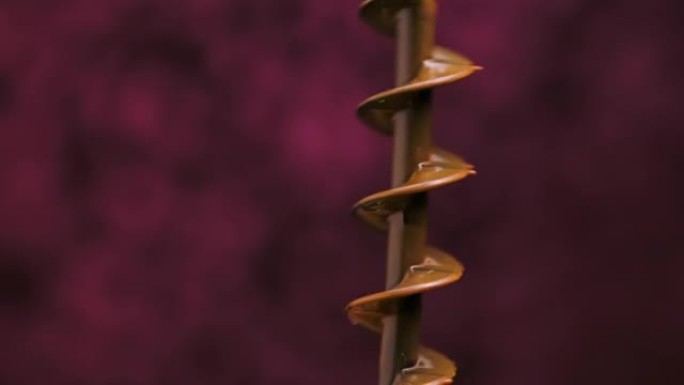 巧克力喷泉的螺旋钻旋转，将融化的巧克力撒在不同的方向上。细节与一滴滴热甜甜点隔离在模糊的紫色背景。特