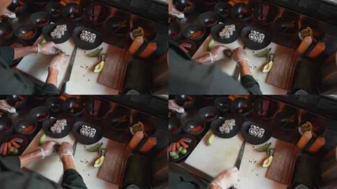 专业厨师在鳄梨切片内滚动饭团。厨师在餐厅为寿司准备蔬菜调味品的俯视图