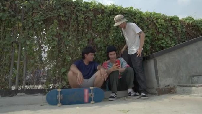 一群朋友在公园白天玩滑板后看着他们的照片和视频