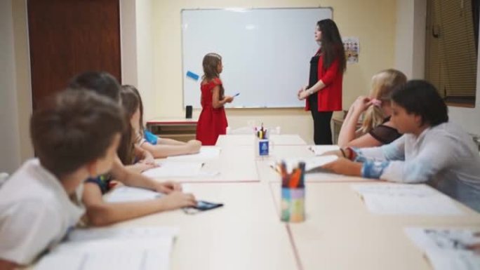 女教师给一个年轻的女学生做记号笔，在黑板上写下答案