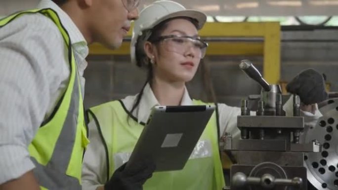 亚洲工程师和技术人员戴着安全护目镜和头盔，在平板电脑上查看机器信息，成功地修复了机器，以恢复工厂的正
