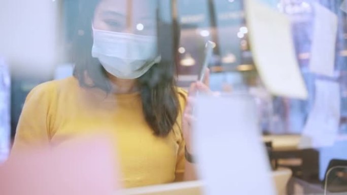 有吸引力的自由职业者亚洲女性创意人士穿着休闲黄布和面罩保护手点并写下办公空间新的生活方式