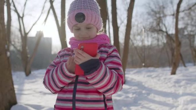 童女在手机上与朋友和家人聊天，冬季公园的远程交流