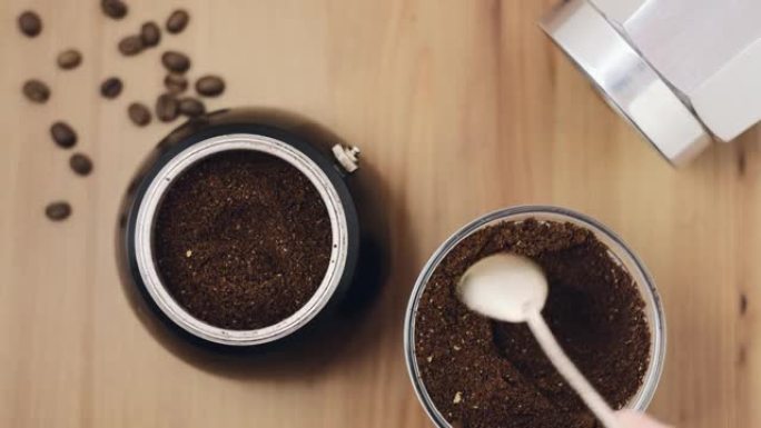 在金属意大利咖啡壶中冲泡浓缩咖啡。磨碎的阿拉比卡咖啡豆，勺子装入咖啡壶，俯视图放在木桌上。咖啡店煮咖