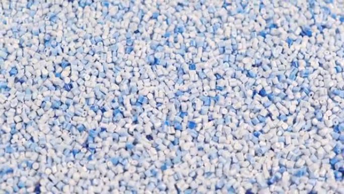 由聚丙烯制成的次级颗粒，浅蓝色的塑料颗粒碎在桌子上。工业用颗粒塑料原料。聚合物树脂。生塑料回收概念。