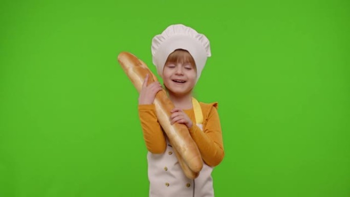 打扮成厨师的女孩小孩表现出嗅着两个新鲜的法式长棍面包，将面包伸到相机上