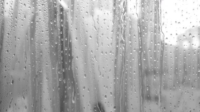 水滴溅到玻璃上。雨天的窗户。湿玻璃，有大滴水或雨水。大雨时，水滴在透明玻璃表面上的黑白视频。滴水