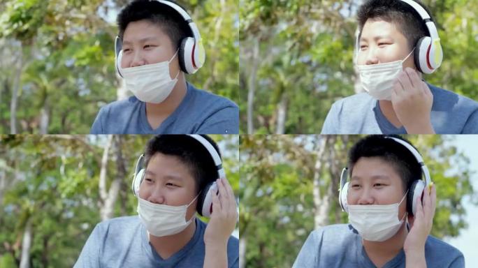 快乐的亚洲男孩戴着口罩，在户外校园里用无线耳机听音乐时摇头，社交距离概念。